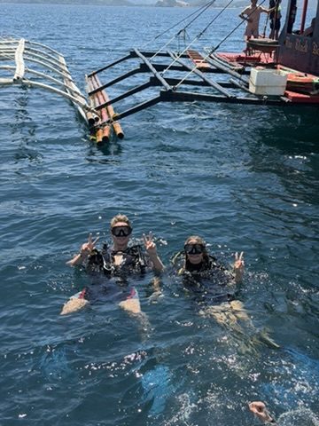 Two divers surfacing near the dive boat throwing peace signs