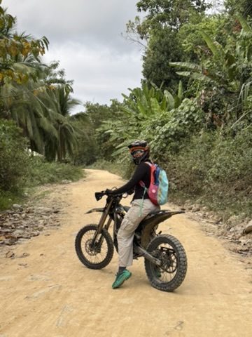 Meg riding a Surron electric dirt bike on a jungle dirt road in Port Barton