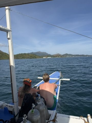 Meg and Ryker sitting on the dive boat outrigger with Coron islands in the background