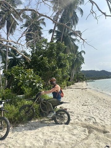 Ryker on a Surron electric dirt bike on a white sand beach in Port Barton