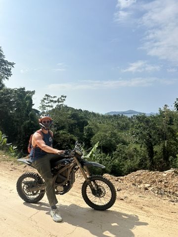 Ryker on a Surron dirt bike at a hilltop overlook with ocean views behind him