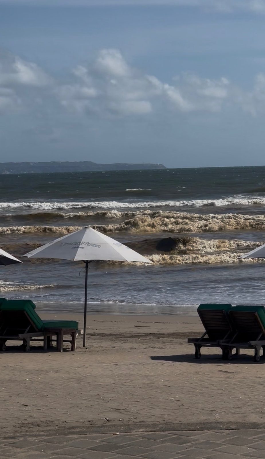 Bali beach with dark brown frothing contaminated waves during wet season, chairs and umbrellas in foreground