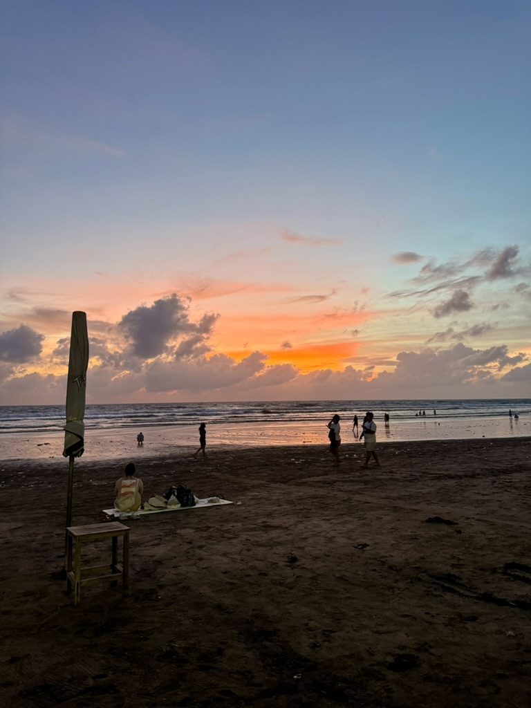 Sweeping Bali beach at sunset with orange and pink sky, silhouetted figures walking the shore