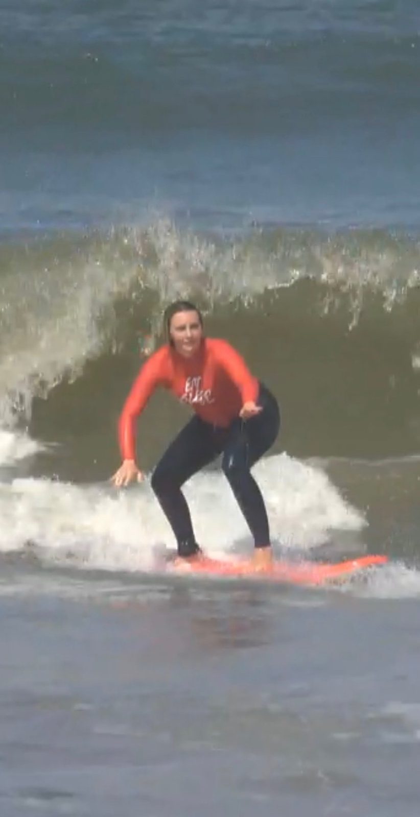 Meg standing on her surfboard riding a wave in the brown contaminated water at Seminyak beach