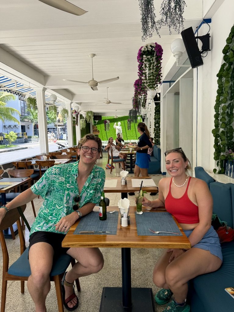 Ryker and Anna smiling at a flowery Bali restaurant over beers and green cocktails