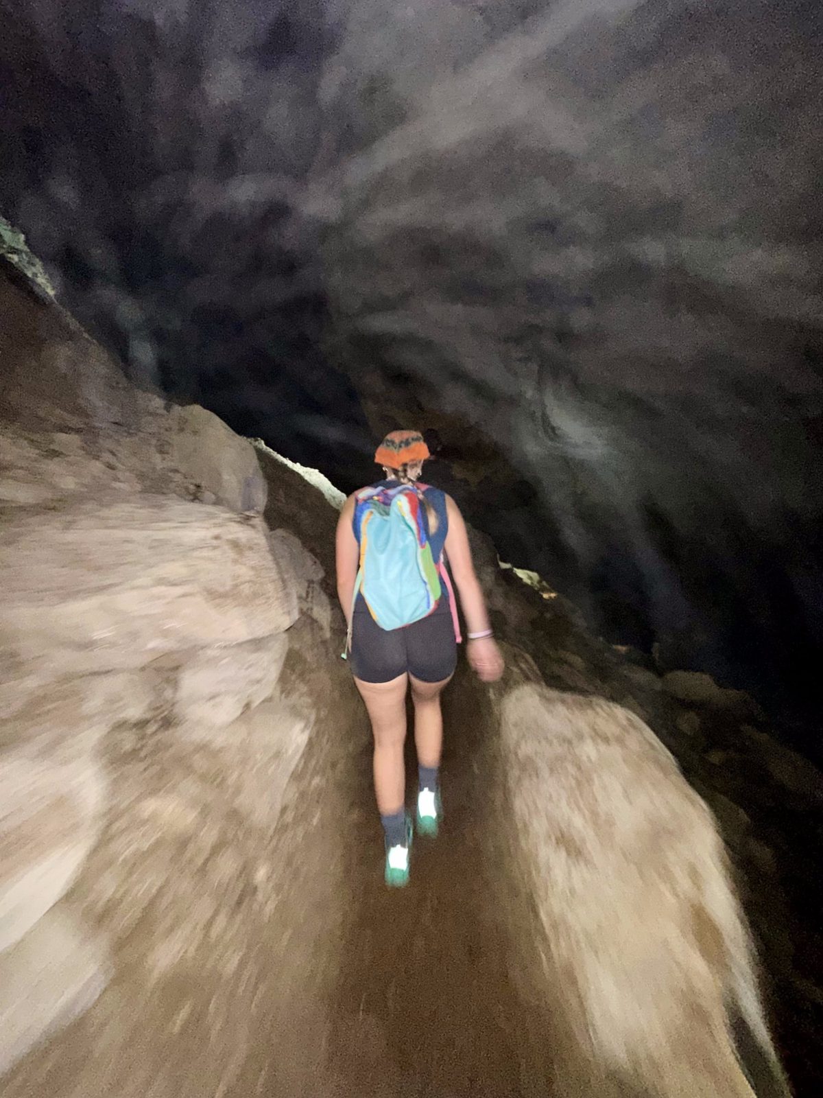Meg walking through a narrow dark cave passage, motion blur, headlamp light on the ancient rock walls