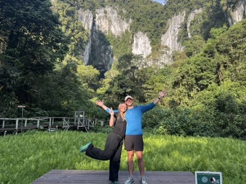 Meg and Ryker arms wide open in front of the dramatic Mulu limestone cliffs and lush green jungle