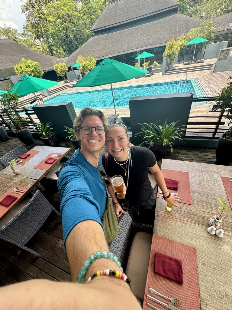 Ryker and Meg selfie at the Marriott Mulu pool restaurant with beers and the lush jungle pool behind them