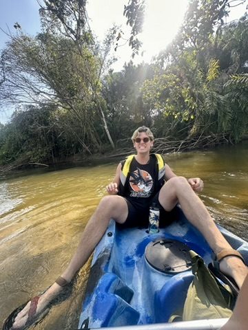 Ryker lounging back in a blue kayak on a jungle river, totally at ease