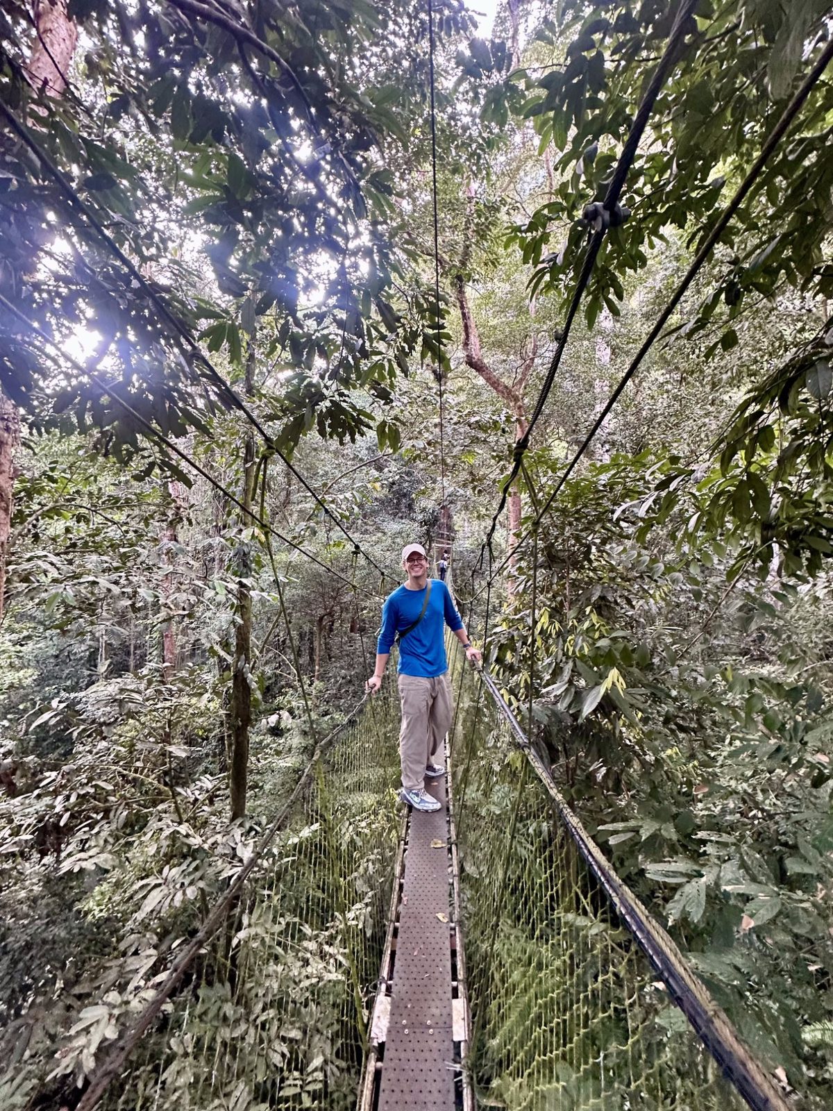 Ryker walking across a long suspension bridge high in the Borneo rainforest canopy