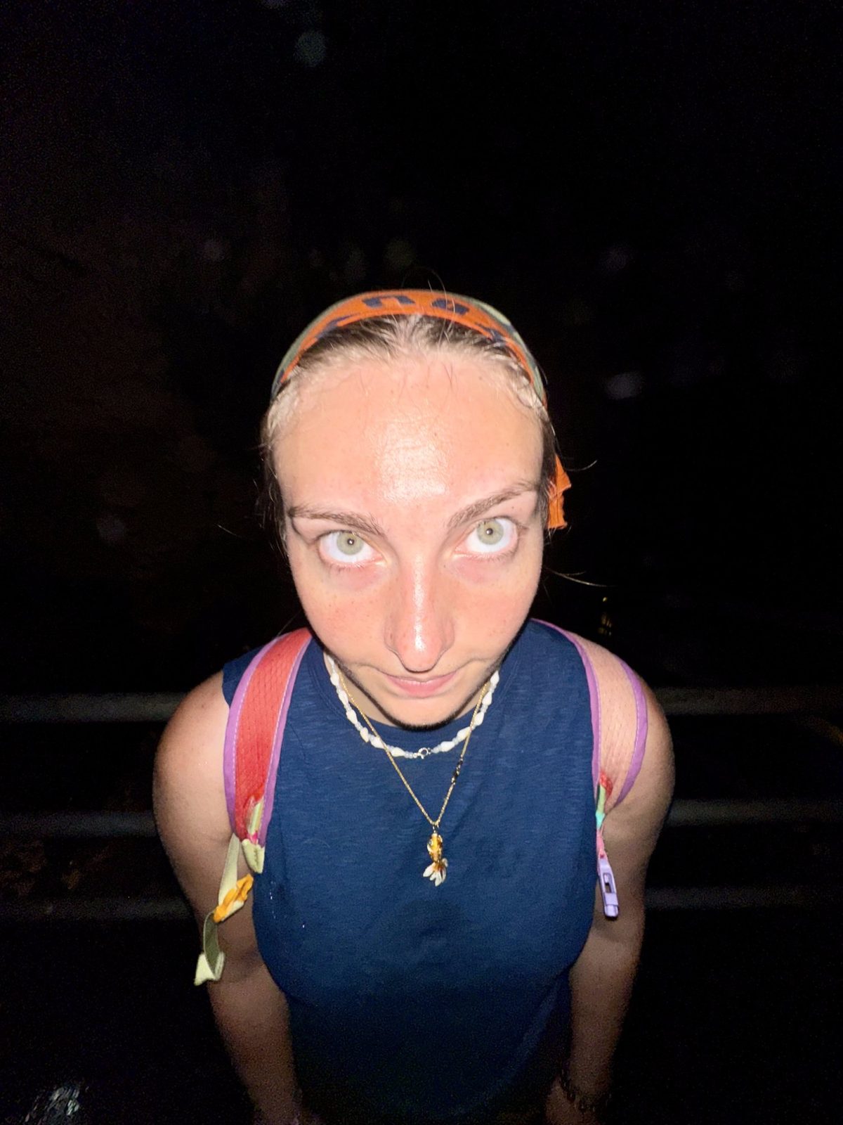 Meg wide-eyed and sweaty staring into the camera in pitch black jungle — pure terror face