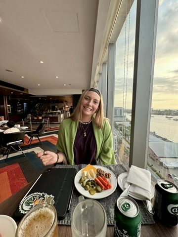 Meg at the Marriott lounge with snacks and a Carlsberg, Kota Kinabalu cityscape and waterfront at sunset behind her