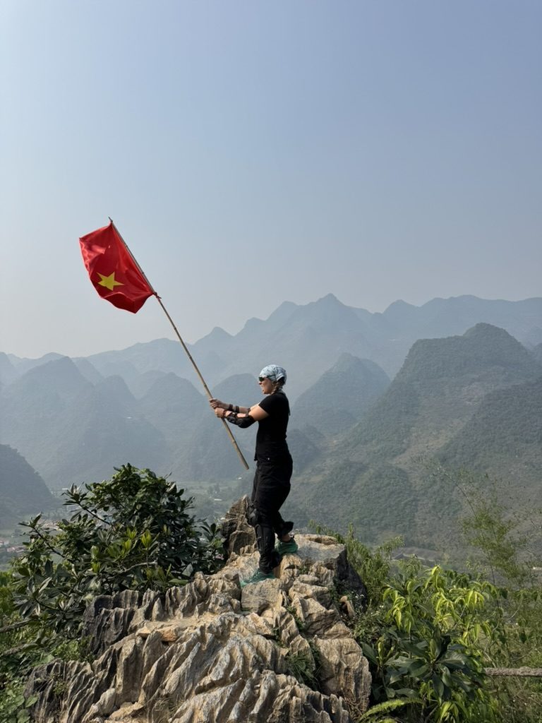 Chantel holding the Vietnam flag on a rocky peak