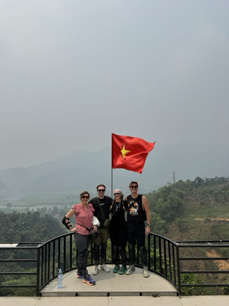 Group photo under the Vietnam flag at a mountain viewpoint