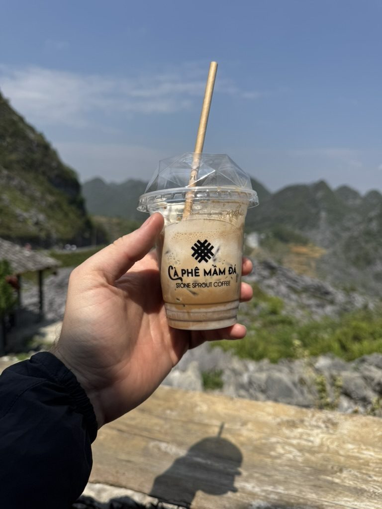 Iced coffee held up against the Ha Giang mountain backdrop