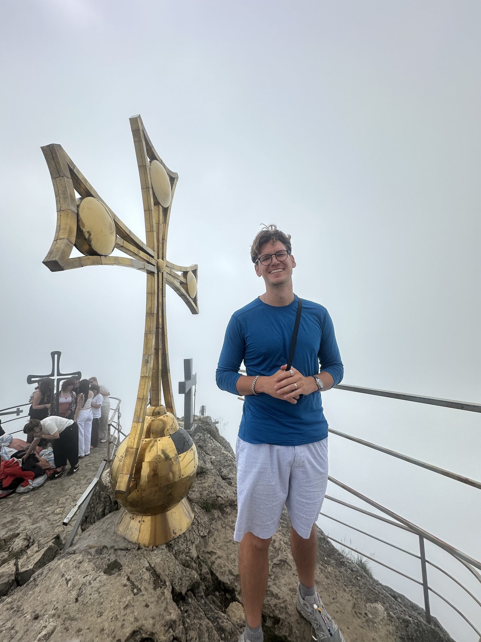 Standing by a golden Georgian cross on a summit