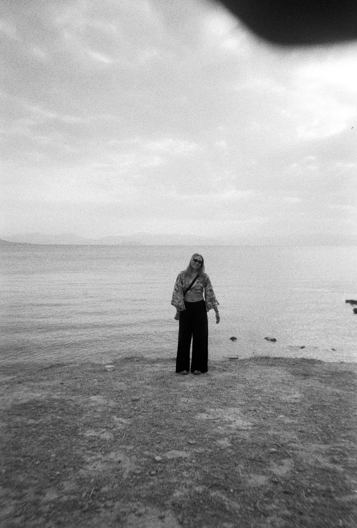 Black and white film photo of Meg standing on a distant beach