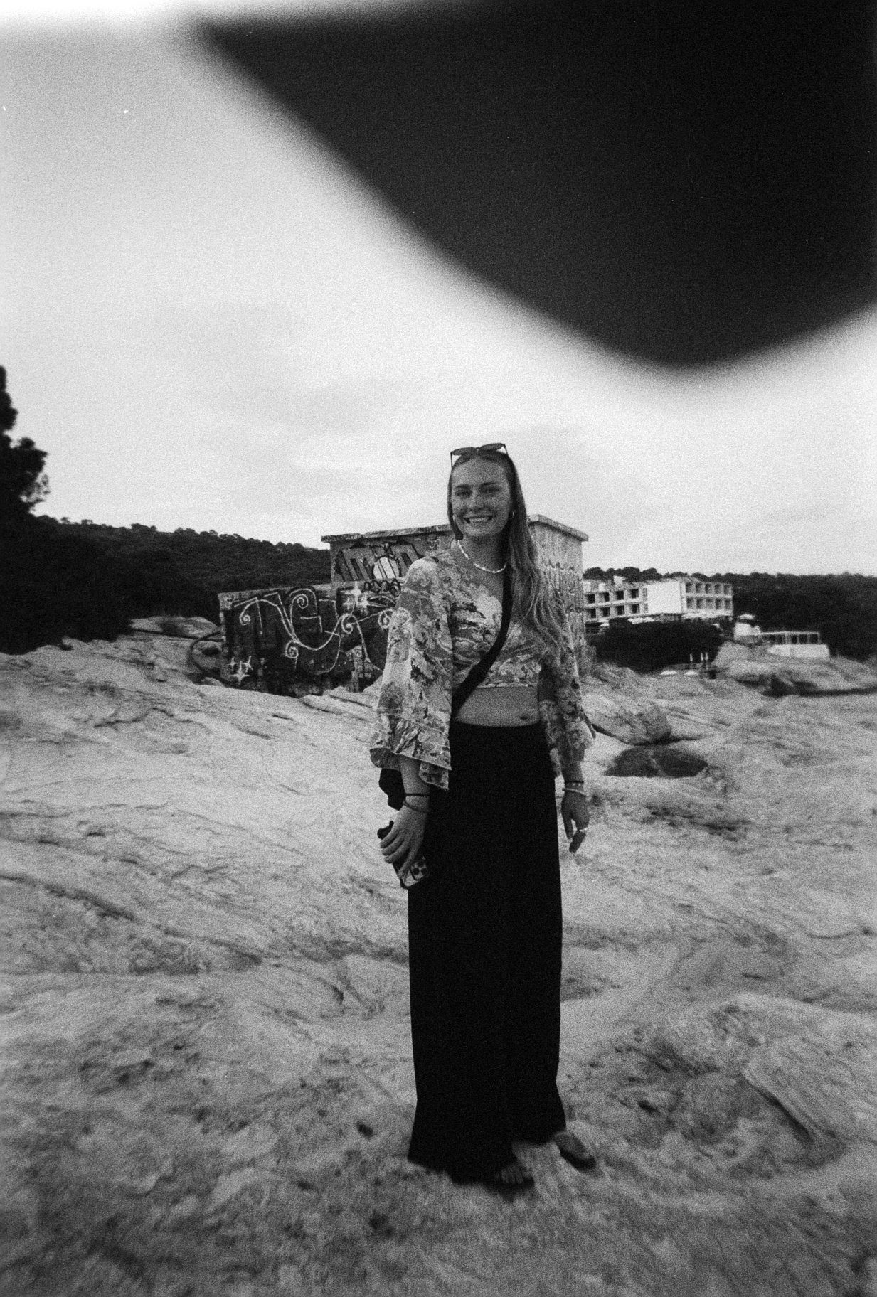 Black and white film photo of Meg standing on rocks with a graffitied building behind her