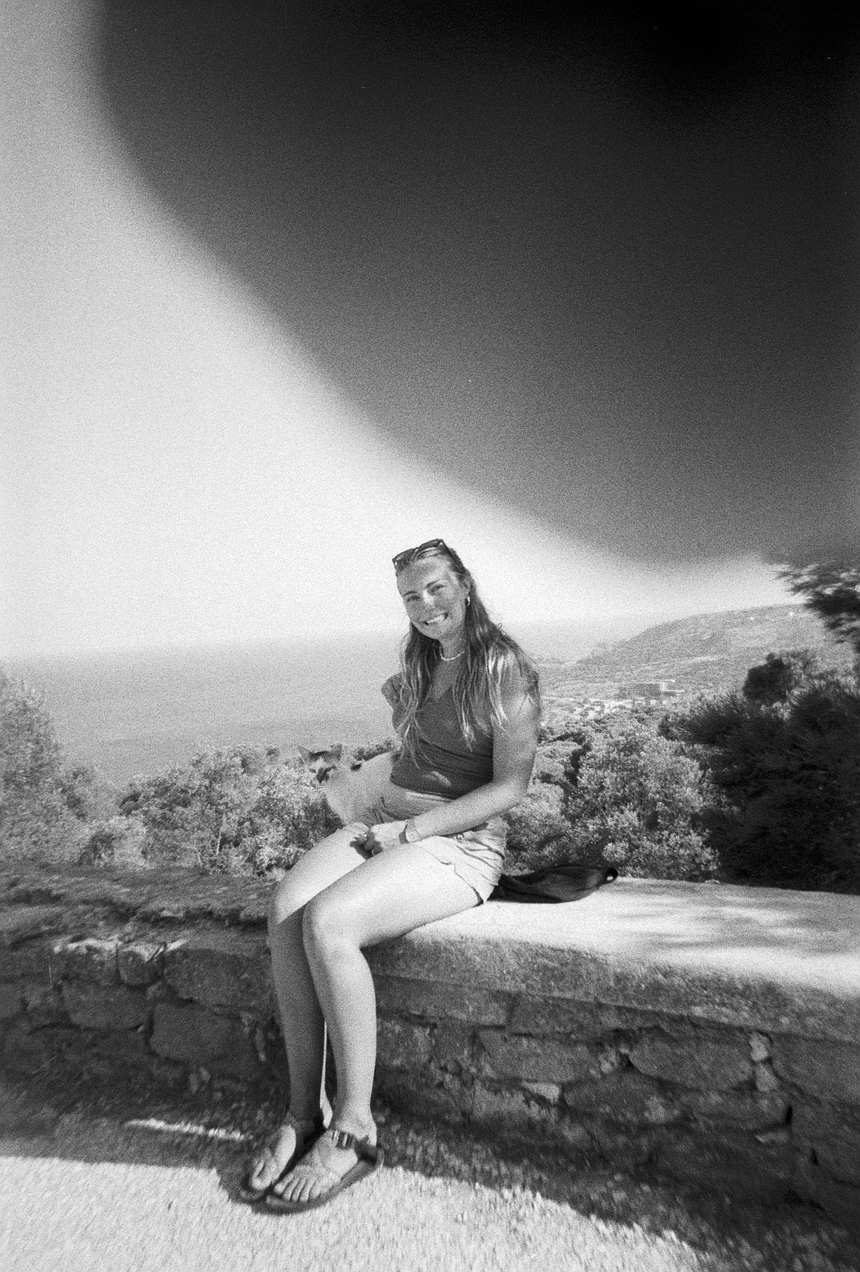 Black and white film photo of Meg sitting on a stone wall