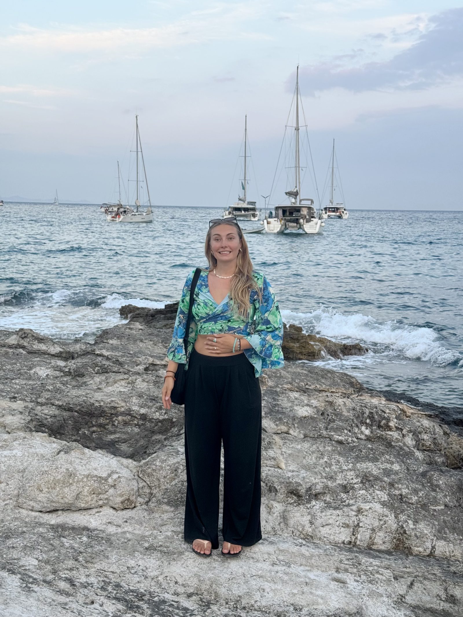 Meg on a rock beach with boats on the sea